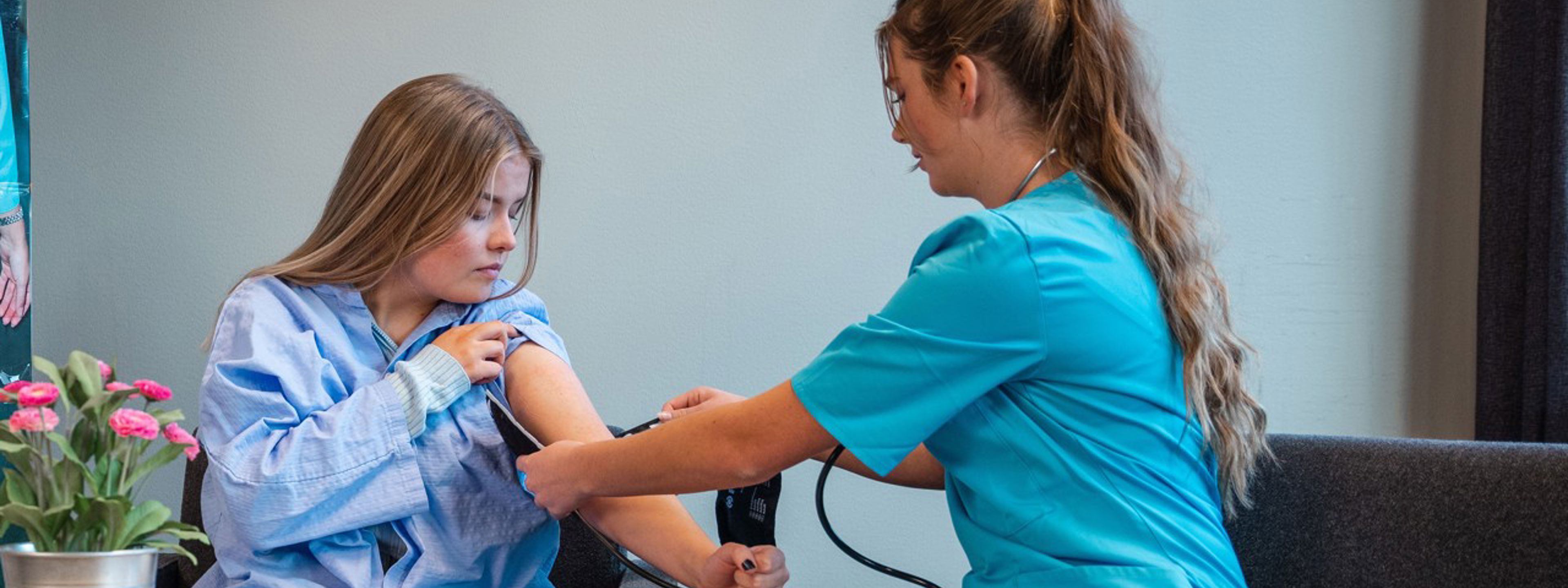 Ei jente har trekt opp skjorta på armen sin og ei helsesjukepleiar sett på henne ei blodtrykk målar