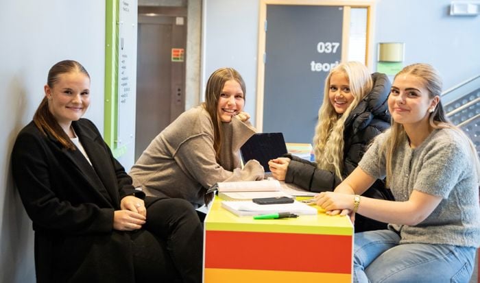 Fire smilande jenter sit ved eit bord og jobbar med skulearbeid.