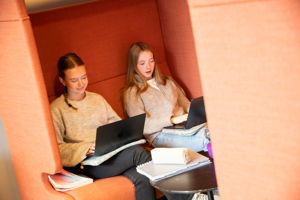 To jenter sit i ein orange sofa og jobbar på kvar sin pc